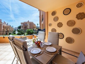 A dining area with a table set for two, a view of the cityscape, and decorative woven wall art. - Baia da Luz - Tropicana Beach Apartment (Luz)