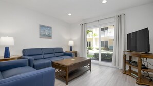 A modern living room with a blue sofa, a wooden coffee table, a TV on a wooden stand, and a painting on the wall.