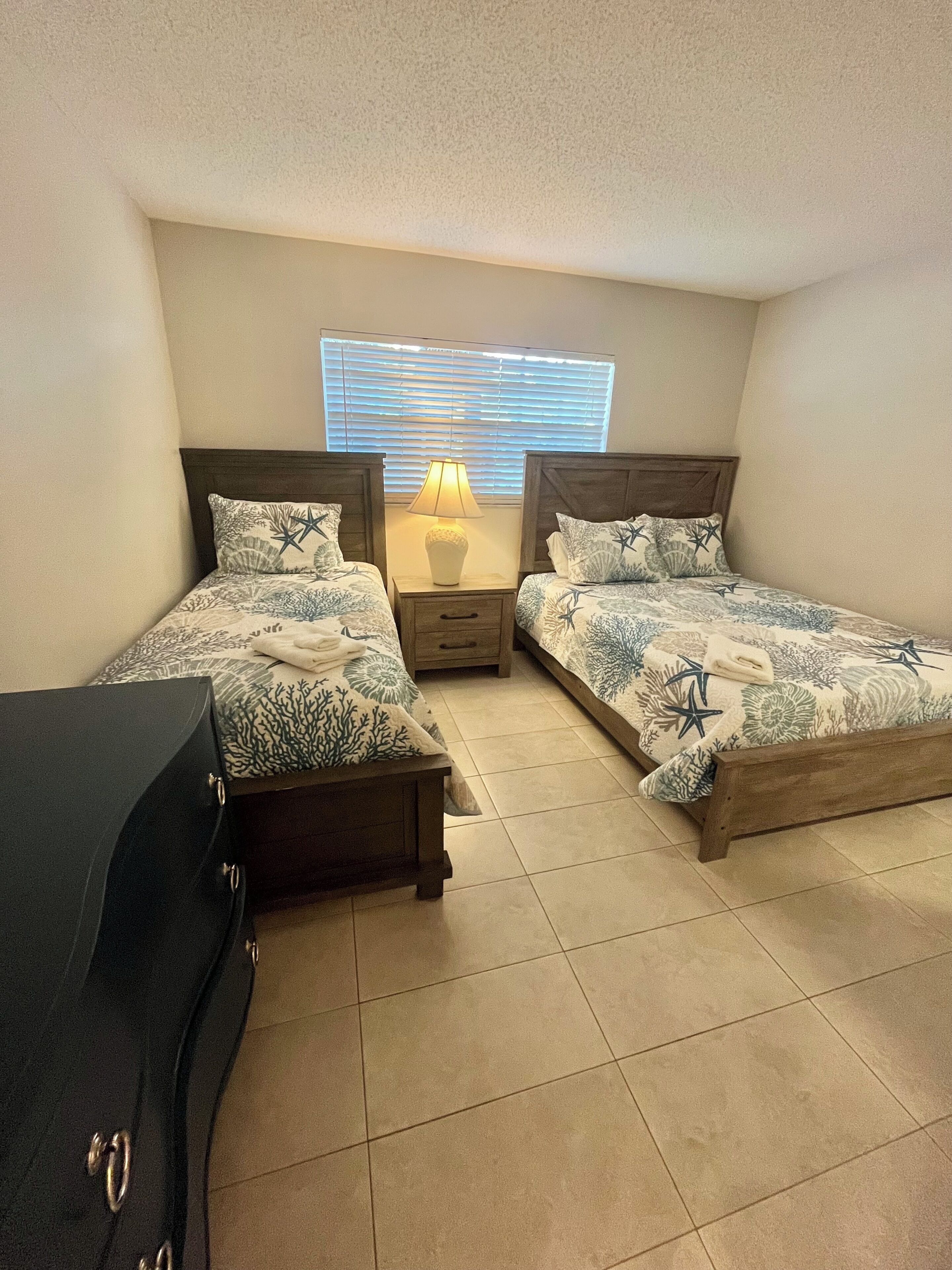 A bedroom with two beds, a nightstand, a lamp, and a dresser.