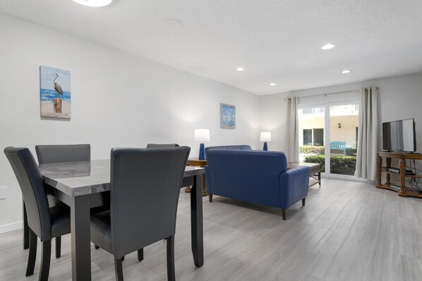 Una sala moderna con una mesa de comedor, un sofá azul y un mueble para televisión.