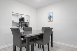 Una cocina moderna con armarios blancos, un microondas negro y un comedor con una mesa de mármol y cuatro sillas.