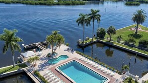 A swimming pool with lounge chairs and palm trees, surrounded by water and greenery.