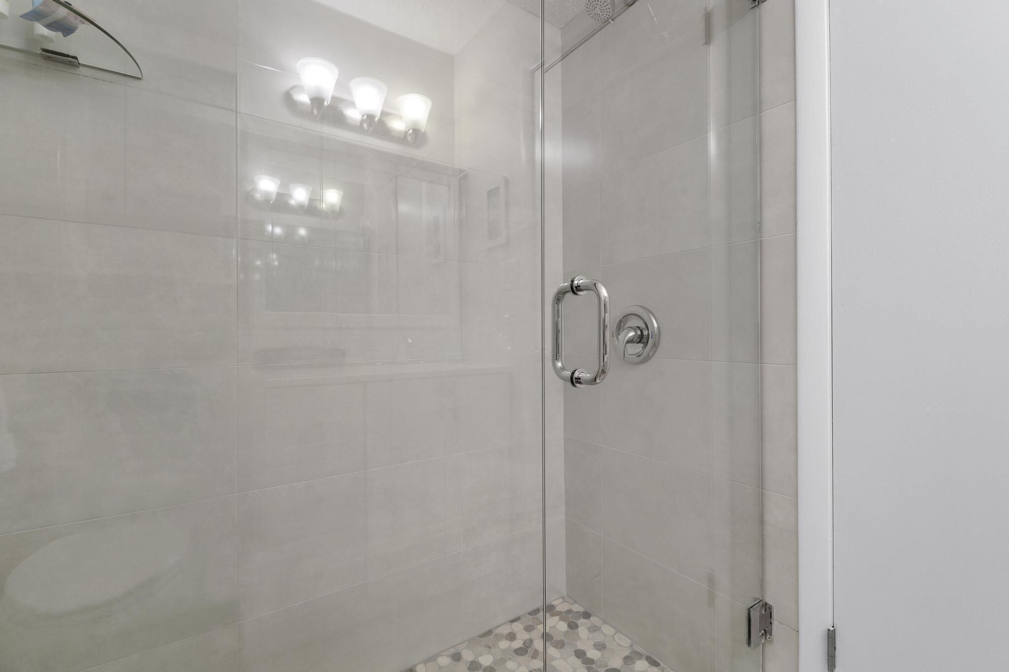 A modern bathroom with a glass shower enclosure, a handrail, and a tiled floor.