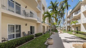 A hotel corridor with balconies, palm trees, and a paved walkway.