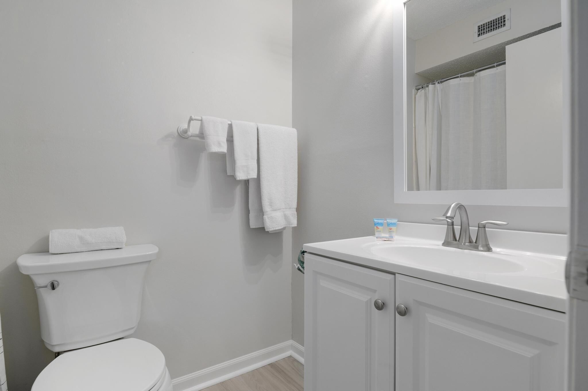 Une salle de bain avec des toilettes, un lavabo avec un miroir et un rideau de douche.