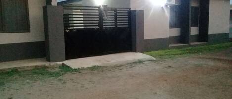 A residential building with a gated entrance, a concrete driveway, and a small grassy area in front.