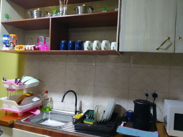 A kitchen with a sink, dish rack, and various kitchen items on shelves.