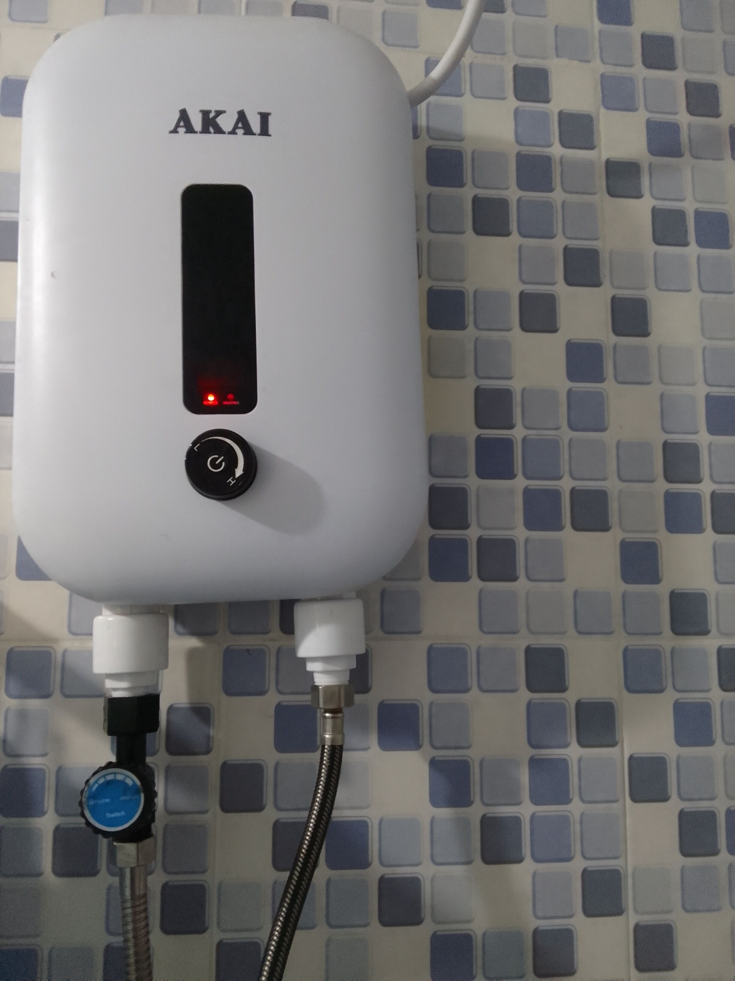 A white device labeled "AKAI" with a red light indicator, connected to a tiled wall with a blue and white pattern.