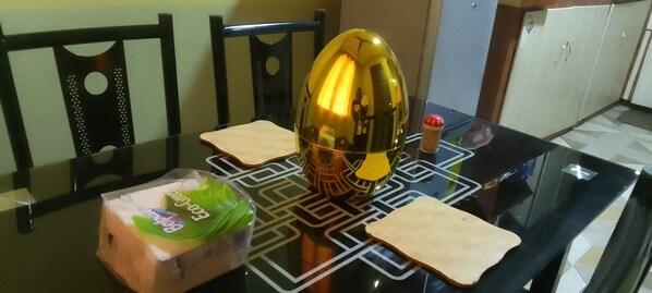 A dining table with a glass top, two wooden placemats, a green packaged food item, and a golden object.