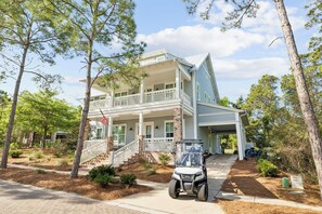 A two-story house with a porch, a vehicle parked in front, and a flag. - Close to the Clubhouse with Bikes and LSV (Santa Rosa Beach)