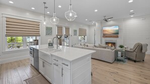A modern kitchen with a central island, pendant lights, and a fireplace in the living area. - Close to the Clubhouse with Bikes and LSV (Santa Rosa Beach)