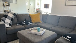 Ein graues Ecksofa mit einer schwarz-weiß karierten Decke, einem gelben Kissen und einer blauen Tasse auf einem Tablett.