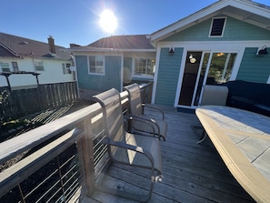 A wooden deck with chairs and a barbecue area, a wooden fence, and a house with a green exterior.