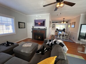 A living room with a fireplace, grey sofas, and a dining area with a table and chairs.