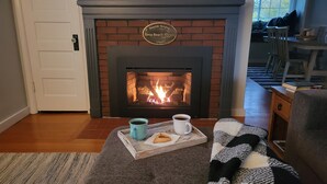 Ein gemütliches Wohnzimmer mit Kamin, einem Tablett mit Tasse und Keks sowie einer Decke auf einer Couch.