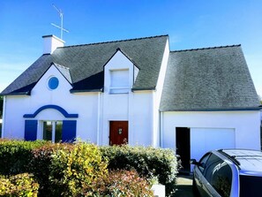 A white building with a grey roof, a red door, and a garage.