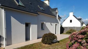 Een modern huis met twee verdiepingen, een witte gevel, een kleine voortuin en een zichtbare schoorsteen.