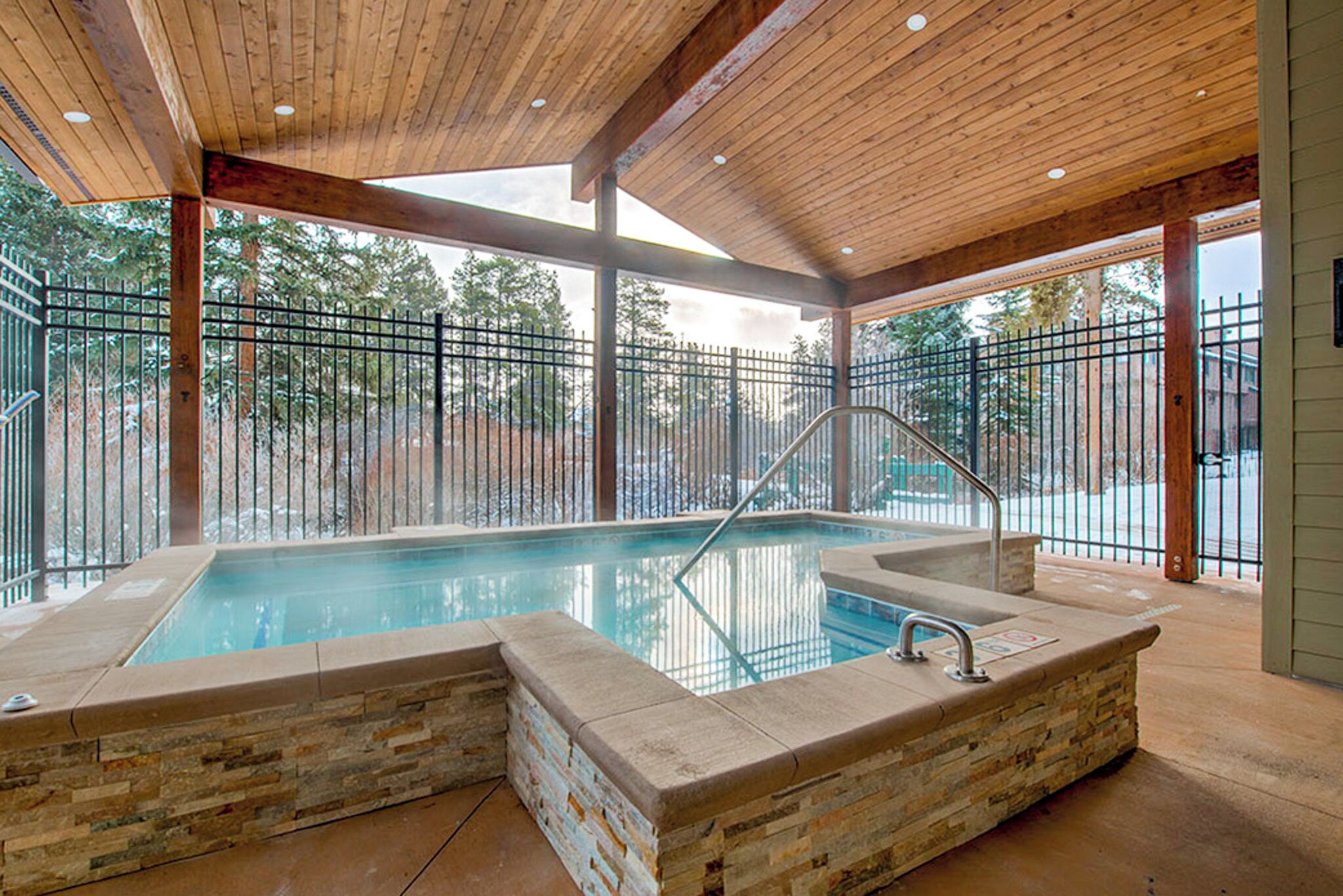 A spa area with a hot tub, stone seating, and a wooden ceiling.