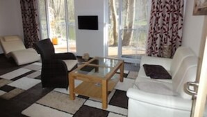 A living room with a checkered floor, a white sofa, a black armchair, and a glass coffee table. - Seebrise house complete, FH Seebrise (Storkow (Mark))