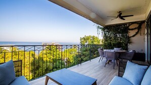 Ein Balkon mit Blick auf das Meer, einem Tisch mit Stühlen und einem Deckenventilator.
