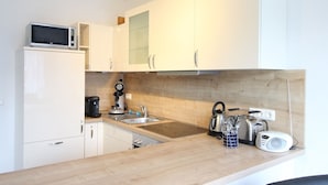 A compact kitchen with white cabinets, a microwave, a coffee maker, and a kettle. - Kurparkcarree - Apartment "Meeresbrise" (Ostseebad Juliusruh)