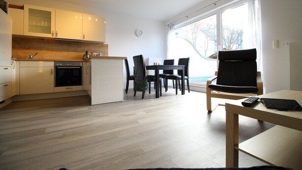 A modern kitchen with a dining area, a small table with a chair, and a large window providing natural light. - Kurparkcarree - Apartment "Meeresbrise" (Ostseebad Juliusruh)