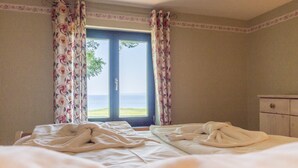 Ett hotellrum med en säng, blommiga gardiner, utsikt över havet och en byrå.