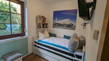 Ein Schlafzimmer mit Bett, Fenster, Bücherregal und Wandfernseher.