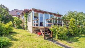 Une maison moderne dotée d’une grande baie vitrée, d’une terrasse en bois et d’un jardin.