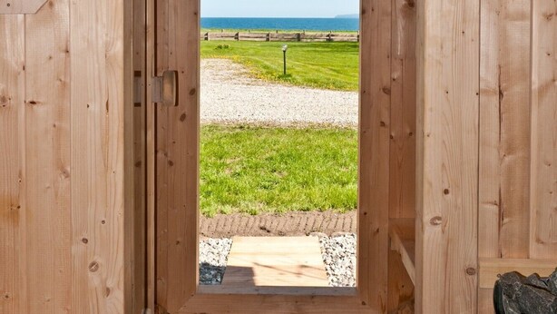 Eine Holzhütte mit freiem Blick auf ein Wiesenfeld und ein Gewässer durch einen Rundbogen.