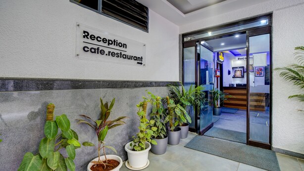 A reception area with a sign for the reception cafe/restaurant, potted plants, and a glass door leading inside. - Hotel Nevesa Inn (Bengaluru)