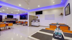 A hotel dining area with tables, chairs, a TV, a sink, and a ceiling fan. - Hotel Nevesa Inn (Bengaluru)