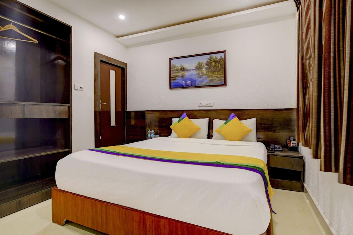 A hotel room with a large bed, a wooden headboard, a painting on the wall, and a curtain on the window.