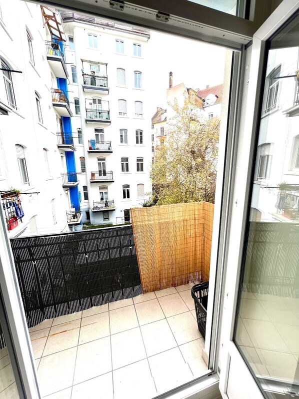 Blick vom Balkon mit Fliesenboden, schwarzem Metallzaun und Holzlattenzaun.