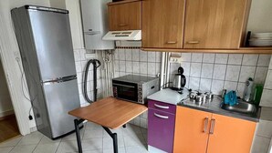 Een kleine keuken met een koelkast, magnetron, fornuis en een houten tafel.