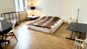 Een slaapkamer met een bed, een klein tafeltje, een stoel, een radiator en een raam.