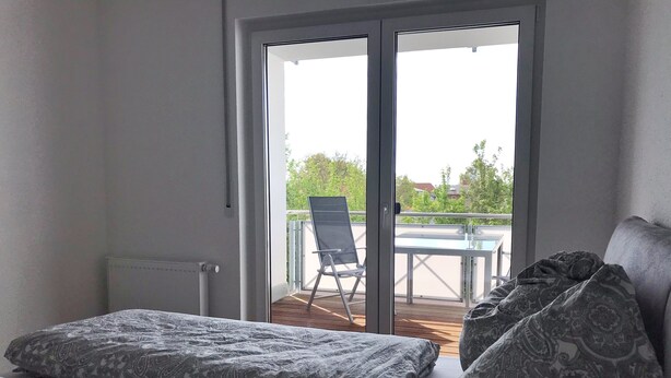 Une chambre avec un lit, une chaise et une vue sur un balcon extérieur équipé d’une table et d’une chaise.