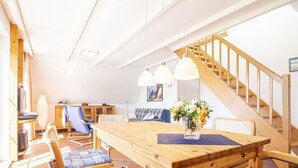 A spacious living area with a wooden dining table, blue patterned chairs, a sofa, and a staircase. - Ferienwohnung "meeresrauschen" (Breege)