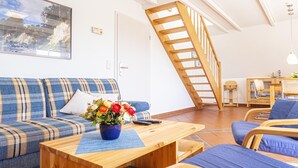 A living room with a sofa, a coffee table with a vase of flowers, a wooden staircase, and a dining area with chairs. - Ferienwohnung "meeresrauschen" (Breege)