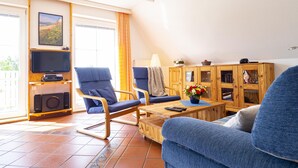 A living room with two blue armchairs, a wooden coffee table, a television, and a cabinet with glass doors. - Ferienwohnung "meeresrauschen" (Breege)