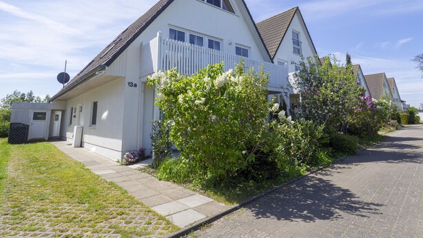 A white two-story house with a sloped roof, a fenced yard, and a paved driveway. - Ferienwohnung "meeresrauschen" (Breege)