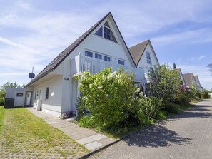 Une maison blanche à deux étages, avec un toit en pente, une cour clôturée et une allée pavée.