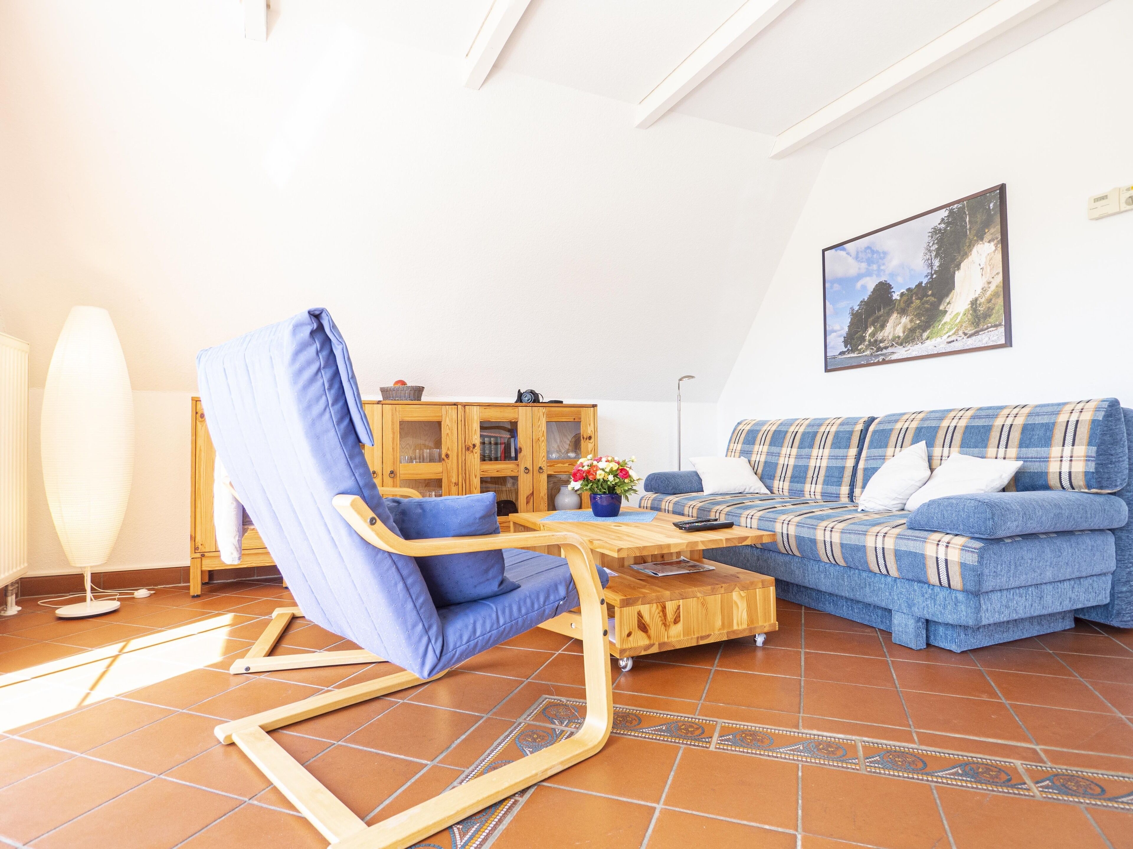 Ein Wohnzimmer mit einem blauen Sofa, einem blauen Sessel, einem Holztisch und einem Fliesenboden.