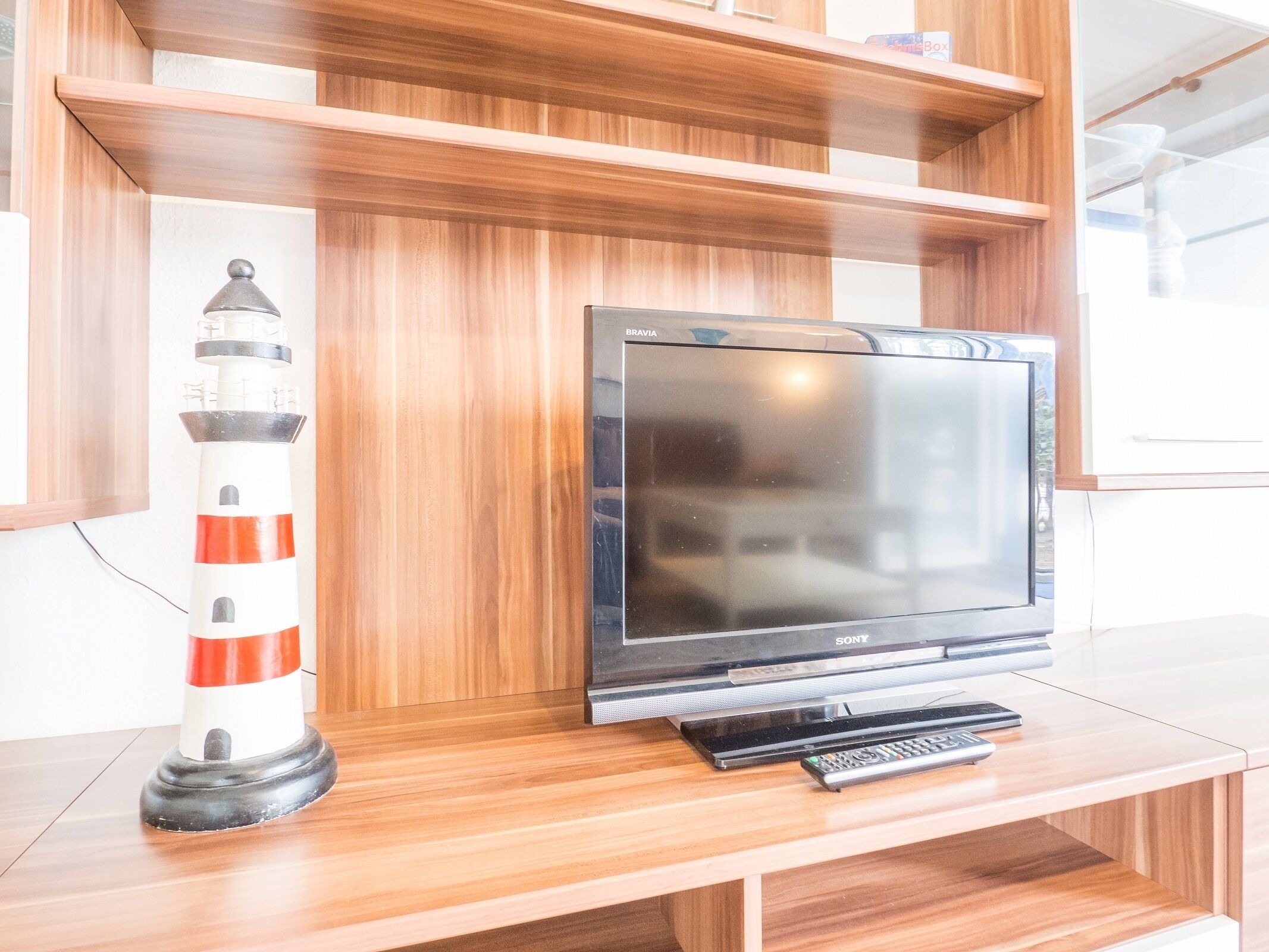 A wooden entertainment unit with a flat-screen TV, a remote control, and a decorative lighthouse.