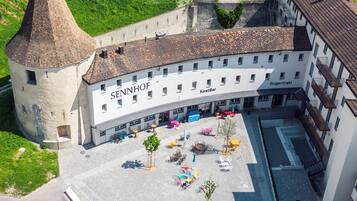 Un patio con asientos al aire libre, un edificio con rótulos que indican 'SENNHOF' y 'KostBar', y una torre de piedra.