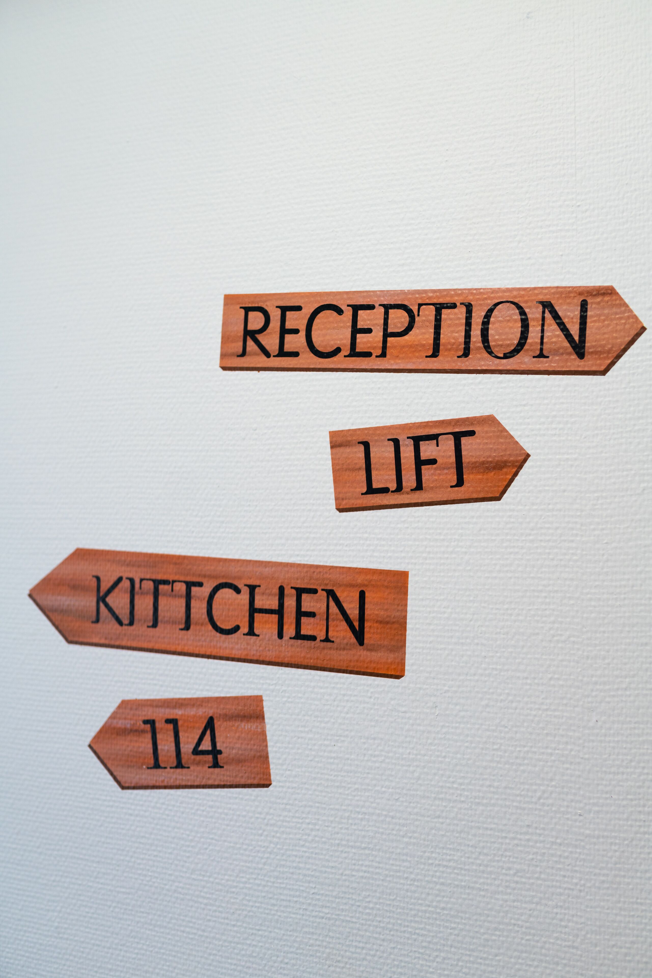 Wooden directional signs with labels "RECEPTION," "LIFT," "KITCHEN," and "114."