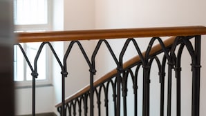 A staircase with a wooden handrail and black metal balusters. - Bogentrakt - Hostel (Chur)