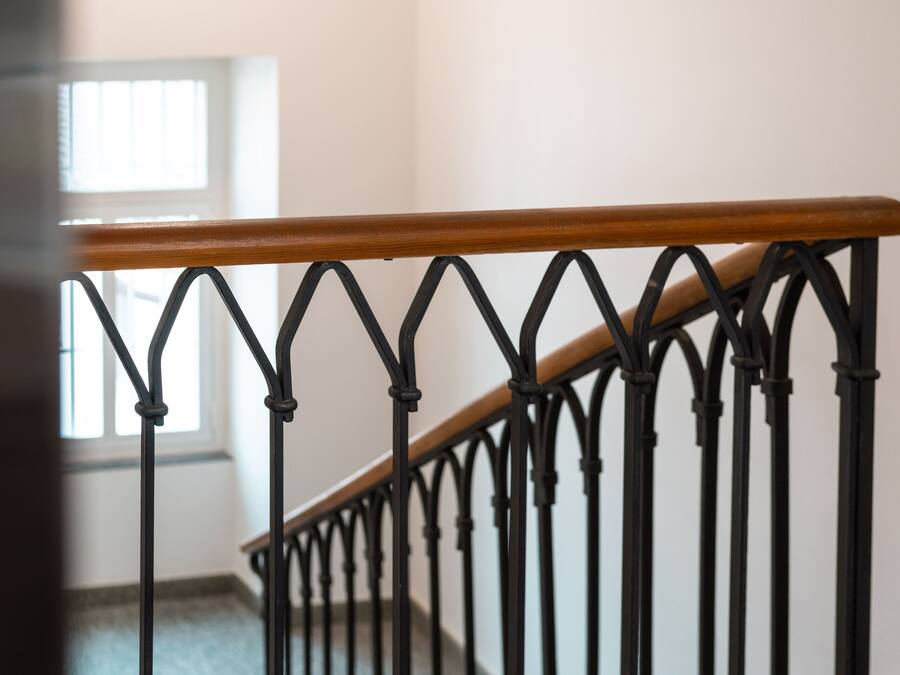 A staircase with a wooden handrail and black metal balusters.