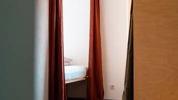 Una habitación pequeña y estrecha con una cama individual y un ventanal cubierto por una cortina roja.