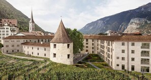 A historic building with a tower, a church, and a mountain backdrop. - Bogentrakt - Hostel (Chur)